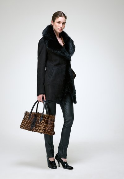 Femme portant un manteau noir à col en fourrure, un pantalon en cuir noir et des talons noirs, tenant un sac à main en fourrure à imprimé léopard marron.