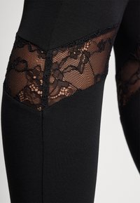 Mustat legginsit, joissa on verkko-osia ja kukkakuvioista pitsiä. Luja kangas, tiukka malli ja kontrastiset pitsikoristeet.