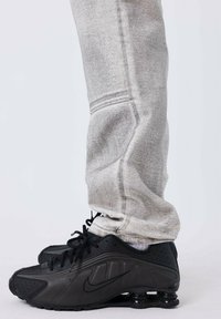Sneakers neri Nike con una texture liscia e una suola arrotondata. Accompagnati da pantaloni della tuta grigi, che mostrano un taglio affusolato e un tessuto morbido.