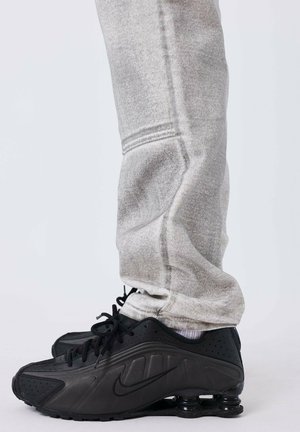 Zwarte Nike sneakers met een gladde textuur en een ronde zool. Vergezeld door grijze sweatpants met een taps toelopende snit en zachte stof.