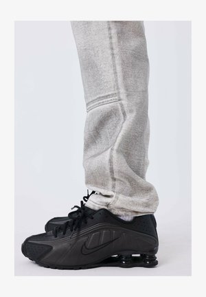 Zwarte Nike sneakers met een gladde textuur en een ronde zool. Vergezeld door grijze sweatpants met een taps toelopende snit en zachte stof.