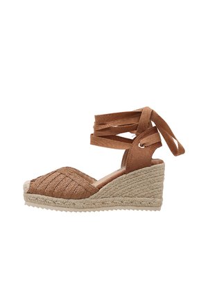 Sandalia cuña de esparto marrón tejido con lazo para atar alrededor del tobillo y suela de cuerda de yute, punta abierta y talón cerrado.