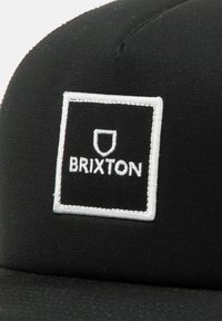 Fekete sapka strukturált dizájnnal, elöl fehér hímzett négyzetlogóval, amelyen a "BRIXTON" felirat található. Sima szövet texture.