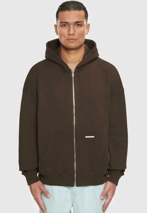 Bruine rits-hoodie met een capuchon, grote voorzakken en geribde manchetten. Gemaakt van zachte stof met een subtiele glans. Etiket op de onderste zak.