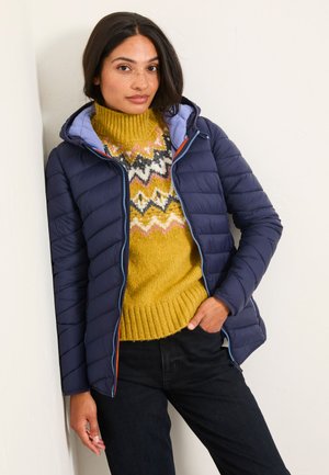 Navy puffer jacket with horizontal quilted pattern, blue lining, and zipper. Layered over a textured yellow and patterned sweater. Black jeans.