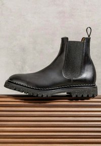 Botte Chelsea en cuir noir avec un panneau latéral élastique, une semelle en caoutchouc texturée, un passant pour tirage, dotée d'une bande de roulement robuste et de coutures discrètes.