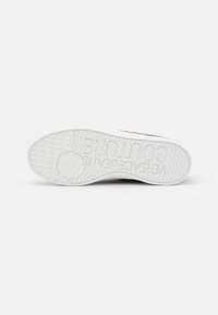 White sneaker sole with textured grip pattern and "VERSACE JEANS COUTURE" embossed on the bottom, displayed against a plain background.