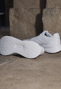 Paar saubere weiße Sportschuhe auf einem Steinboden, ein Schuh zeigt die strukturierte Sohle, der andere die Seitenansicht.