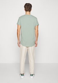 T-shirt en coton vert menthe à manches courtes, avec un col rond et un ourlet arrondi, assorti à un pantalon beige clair et des baskets blanches.