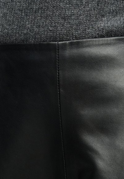 Κοντινή λήψη μαύρου δέρματος και σκουρόχρωμου γκρι ύφανσης μαλλιού ραμμένα μαζί, που δείχνει την υφή και τις λεπτομέρειες της ραφής.