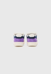 Deux baskets avec une combinaison de bleu marine, de daim violet et d'accents crème. Présentent une semelle texturée et un design arrondi.
