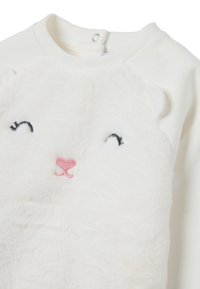 Sweatshirt en polaire blanche mettant en avant un visage d'ours avec des yeux noirs brodés et un nez en forme de cœur rose ; col rond avec fermeture à boutons-pression.