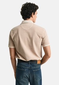Beige kortärmad polo skjorta med krage och cirkulär ryggdetalj, ihop med mörkblå denimjeans och ett svart flätat bälte.