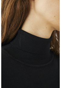 Maglione nero a collo alto in maglia con texture a coste sul collo e sul corpo. Inquadratura ravvicinata dell'area del collo e dei capelli circostanti.