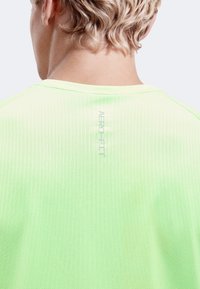 Personne blonde vue de dos portant un maillot de sport texturé AERO FIT vert clair avec des cheveux courts.