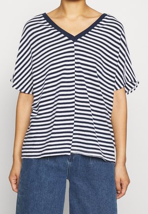 Mujer con una camiseta de manga corta de cuello en V con rayas horizontales azul marino y blancas, combinada con vaqueros azules de mezclilla.