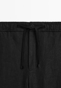 Black linen shorts with an elastic waistband, drawstring closure, and a single button detail at the front. Smooth texture and tailored design.