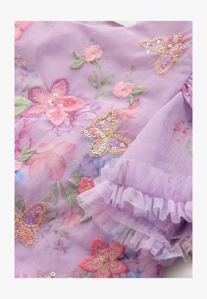 Alyvinė medžiaga su išsiuvinėtais gėlėmis ir drugeliais rožinės ir žalios spalvų, puošta blizgučiais ir raukšlėtais kraštais.