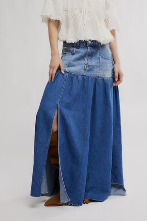 Frau trägt einen zweifarbigen Denim-Maxirock mit einem vorderen Schlitz, kombiniert mit braunen Stiefeln und einer weißen bestickten Bluse.