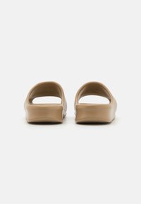 Tan instappers met een glad, rond ontwerp, open achterkant en een gestructureerde zool voor grip. Gemaakt van flexibel materiaal voor comfort.