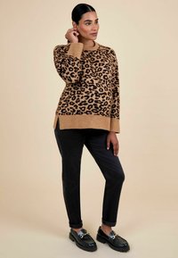 Pull en imprimé léopard marron et noir, coupe ample, ourlets et manches côtelés, porté avec un pantalon noir et des mocassins noirs avec des accents dorés.