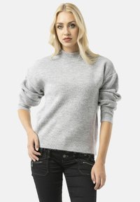 Lichtgrijze geribde trui met een hoge hals en oversized mouwen, gecombineerd met zwarte jeans met ritszakken.