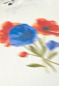 Witte katoenen t-shirt met een vage bloemenprint in blauw, oranje en groene kleuren, met klaprozen en abstracte vormen.