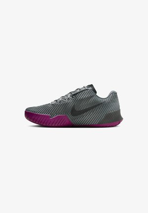 Chaussure de sport grise avec des rainures verticales, des accents noirs et une semelle extérieure violette. Présente un bout arrondi et un système de laçage.