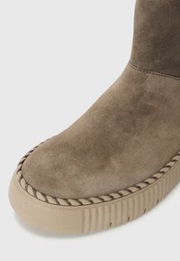 Stivaletto in suede marrone con punta rotonda, caratterizzato da una cucitura e una suola in gomma testurizzata con scanalature verticali.