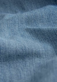 Vaaleansininen farkkukangas, jossa on hienovarainen twill-kuvio, pehmeä rakenne ja kevyet rypyt, jotka heijastavat tyypillisiä farkuille ominaisia piirteitä.