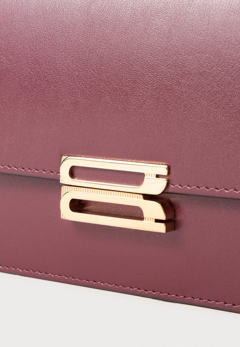 Sac en cuir bordeaux avec une texture lisse, doté d'un fermoir géométrique en or et de coutures contrastantes le long de la couture.