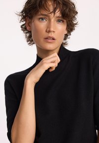 Czarny, lekki sweter z dzianiny o wysokim kołnierzu i krótkich rękawach. Tekstura wydaje się miękka i gładka. Minimalistyczny design.