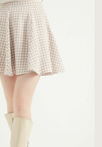 Sukně s potiskem houndstooth v béžové barvě s rozšířeným střihem, vyrobená z lehkého materiálu. Disponuje hladkým povrchem a délkou do poloviny stehna.