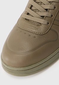 Sneaker in pelle verde oliva con finitura testurizzata, punta arrotondata, cuciture in evidenza e design liscio con lacci. Sottile perforazione vicino alla punta.