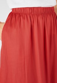 Falda roja con cintura elástica y bolsillos laterales. Hecha de una tela ligera, con una textura suave y fluida.