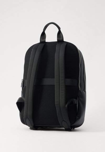 Sac à dos noir avec un dos en tissu en maille, des bretelles rembourrées et ajustables, une poignée supérieure et une fermeture éclair latérale pour un accès facile. Design élégant avec des bords arrondis.