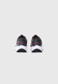Une paire de chaussures de sport noires et roses vue de l'arrière, avec des semelles intermédiaires blanches et des semelles extérieures noires texturées sur un fond uni.