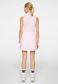 Ärmelloses rosa Golfkleid mit Kragen und taillierter Passform, kombiniert mit weißen Handschuhen, schwarz-weißen Socken und Sportschuhen.