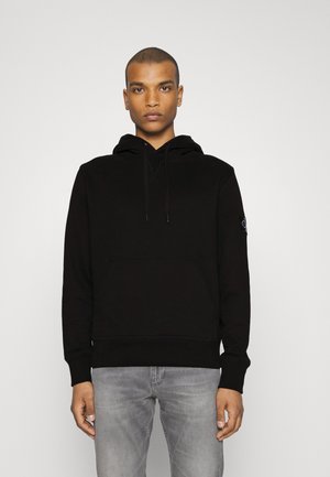 Hoodie in cotone nero con tasca a marsupio, cappuccio regolabile con cordino, polsini a costine e dettaglio a toppa sulla manica sinistra.