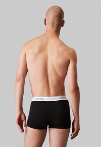 Schwarze Boxershorts mit einem weißen Bund, auf dem das "Calvin Klein"-Logo aufgedruckt ist. Glattes Material, eng anliegende Passform und keine sichtbaren Muster oder Akzente.