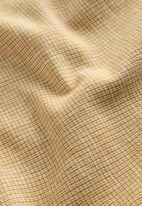 Gros plan d'un tissu beige et blanc tissé avec un petit motif à carreaux et des plis doux.