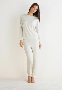 Lys grå loungewear sæt bestående af en langærmet bluse med rund hals og matchende tilspidsede bukser med ribkant ved anklerne. Blødt stof.