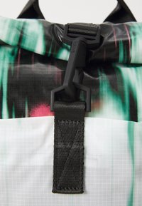 Sac imperméable avec un motif abstrait noir et vert, doté d'une sangle texturée et d'une boucle en plastique noir pour la fermeture.