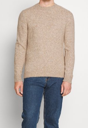 Maglione color marrone chiaro realizzato in un tessuto a maglia testurizzato, con scollo a girocollo, polsini e orlo a costine, abbinato a jeans in denim blu.