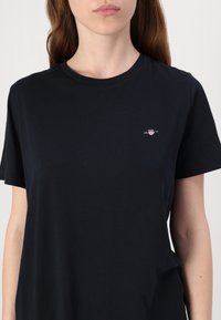 T-shirt in cotone navy con collo rotondo, maniche corte e un piccolo logo sul petto. Tessuto morbido e vestibilità rilassata.