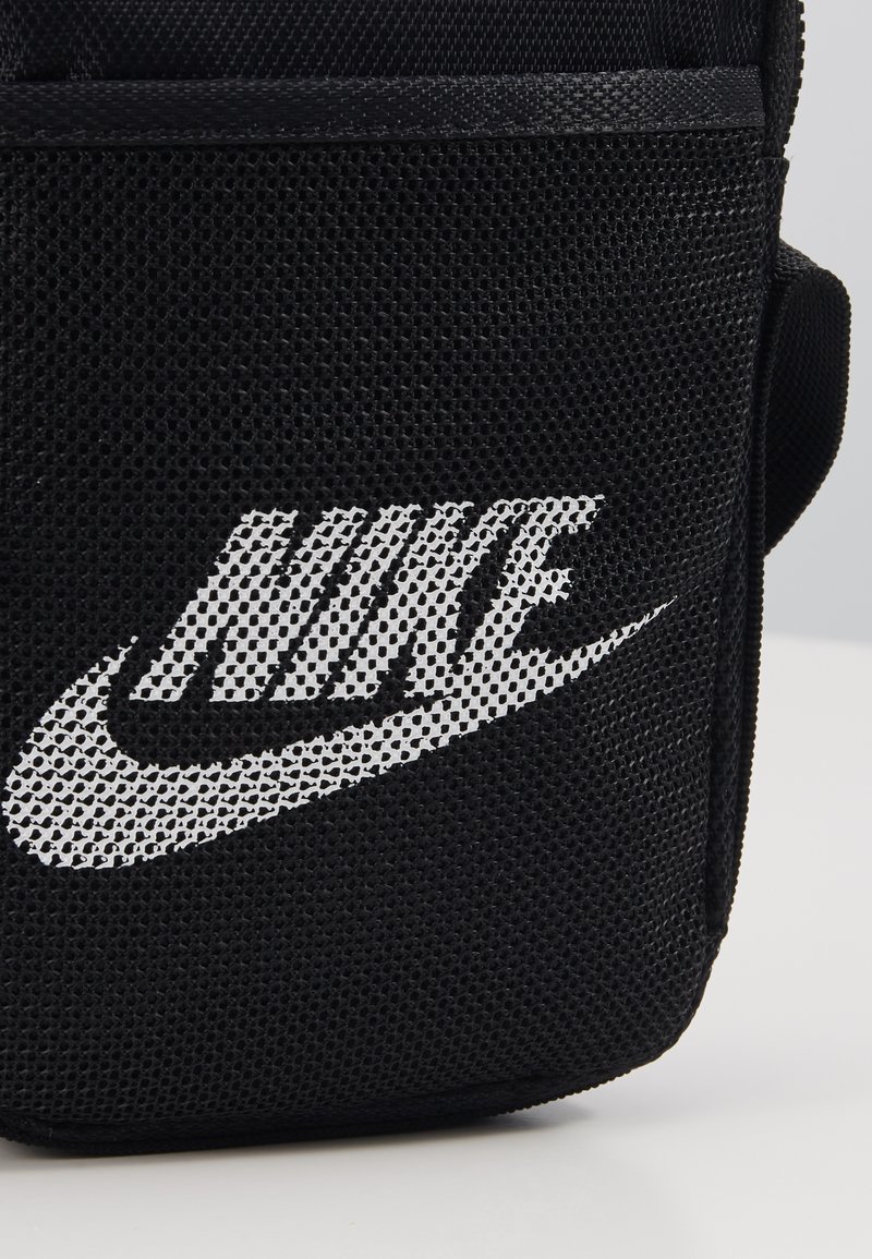 Sac à épaule en mesh noir avec un grand logo Nike blanc. La texture est respirante, avec une forme rectangulaire compacte et une sangle réglable.