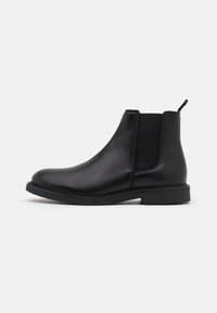 Botte Chelsea en cuir noir avec panneaux latéraux élastiques, texture lisse, bout arrondi et semelle en caoutchouc basse. Comprend une languette de tirage au talon.