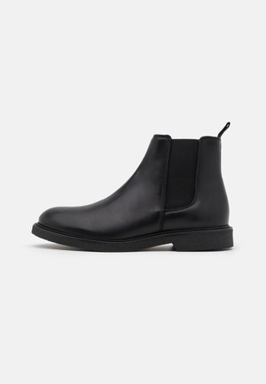 Botte Chelsea en cuir noir avec panneaux latéraux élastiques, texture lisse, bout arrondi et semelle en caoutchouc basse. Comprend une languette de tirage au talon.