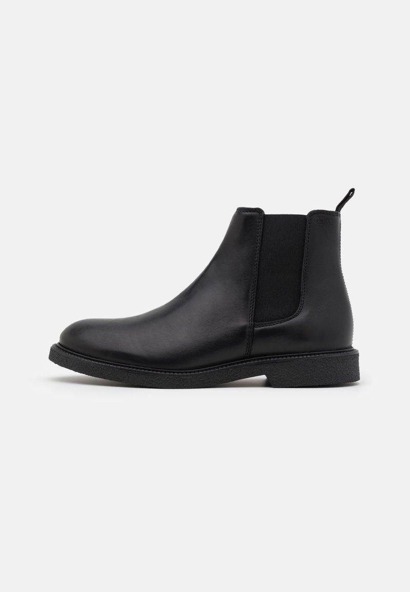 Botte Chelsea en cuir noir avec panneaux latéraux élastiques, texture lisse, bout arrondi et semelle en caoutchouc basse. Comprend une languette de tirage au talon.