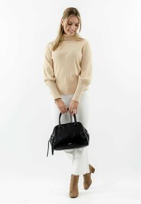 Schwarze Lederhandtasche mit abgerundeten Obergriffen, Reißverschluss und subtiler Logodetail. Getragen mit beigem geripptem Pullover und weißen Jeans.